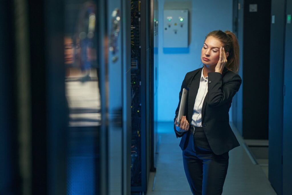 IT manager holding temple in server room to represent losses caused by downtime and lost productivity